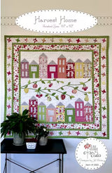 Front cover of the 'Harvest Home' quilt pattern by Jill Finley for Jillily Studio, showing a completed square quilt with a center layout of fabric-pieced houses and appliqued apple trees, surrounded by a pieced geometric star block border.