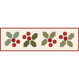 A close-up view of the pieced Holly-Day Cheer holiday runner under soft silver studio lighting, highlighting the clean seam lines and crisp cotton texture of the festive motifs.