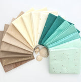 Sandy Toes 17-piece fabric bundle fanned out to show a gradient of tan, cream, aqua, and teal Riley Blake Designs basic fabrics.
