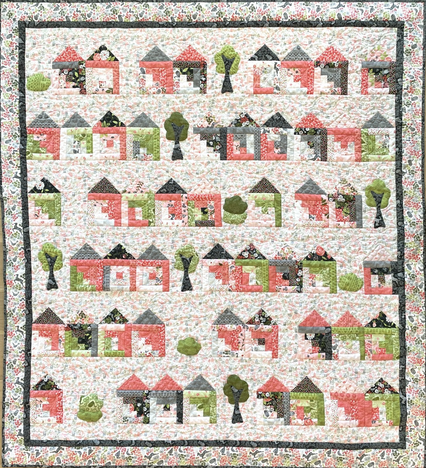 Flat Lay of the finished quilt made with the 'Tiny House Craze' quilt pattern by Jill Finley for Jillily Studio, showcasing a completed quilt featuring a grid of colorful, scrappy log cabin house blocks interspersed with simple appliqued green trees and shrubs.